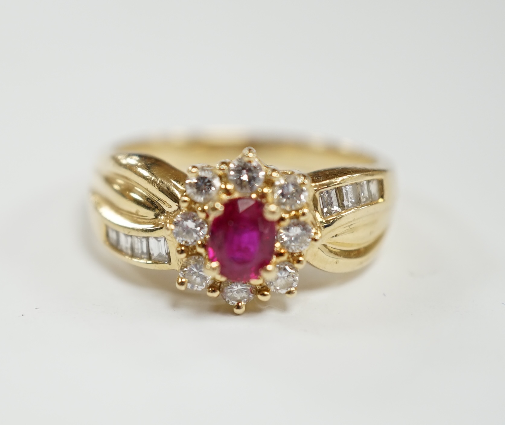 A modern 14k, ruby and diamond set oval cluster dress ring, with diamond chip set shoulders, size P, gross weight 5.1 grams.